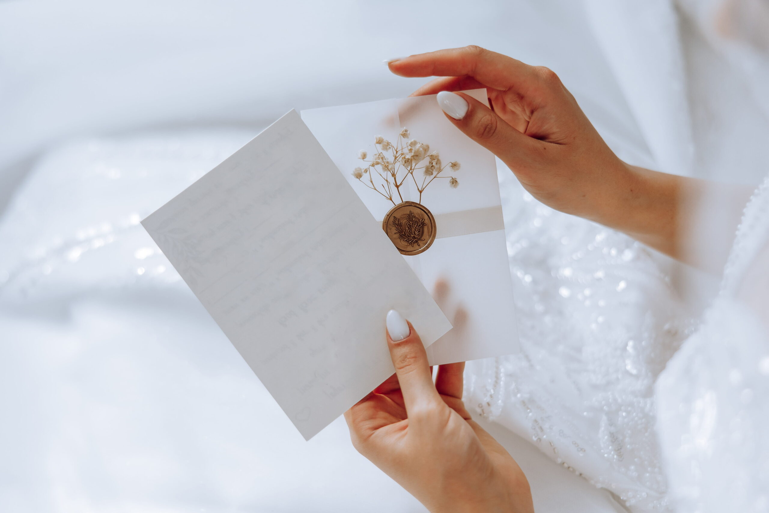 novia sosteniendo una carta dentro de un sobre blanco sellado con lacre y flores secas, detalle íntimo de regalos para el día de la boda